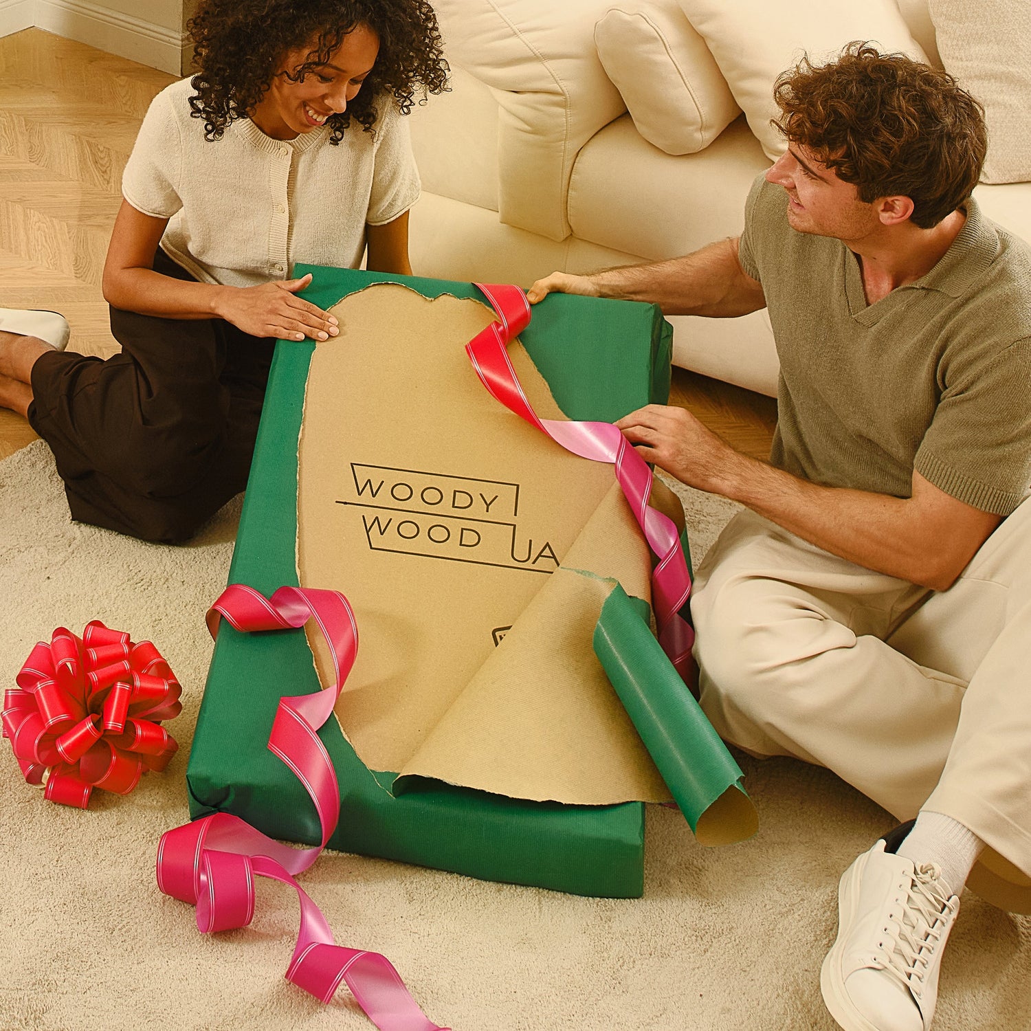 Two people opening a large gift box with 'WoodyWoodUA' branding on a carpeted floor.